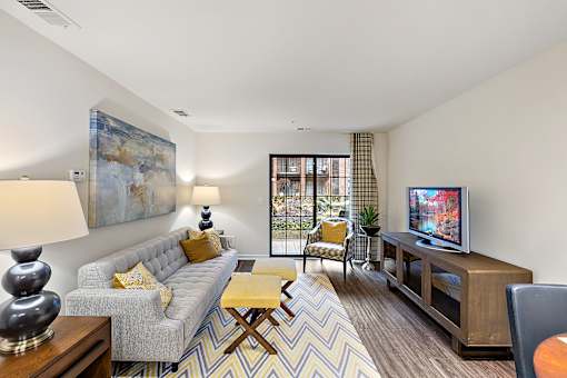 A living room with a grey couch, a yellow cushion, a wooden coffee table, a television, and a painting on the wall at MainCentre, Northville