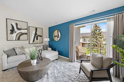 A living room with a white couch, a coffee table, and a large window with a view of a house and trees outside at Briarcliff Village, Michigan, 48390