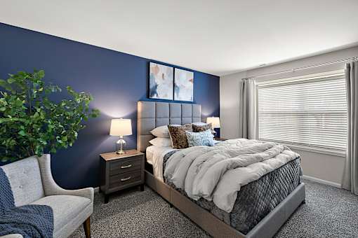 A bedroom with a bed, nightstand, chair, and a plant at Briarcliff Village, Michigan, 48390