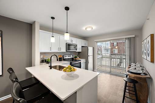 A modern kitchen with a white island and black chairs.