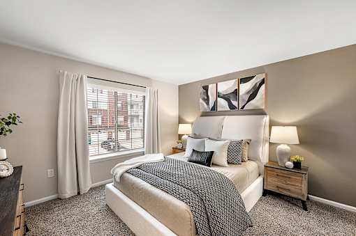 A bedroom with a large bed and a window with white curtains.