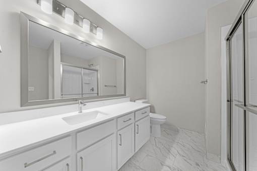 A bathroom with a sink, mirror, toilet, and a walk-in shower at Amberly Apartments, West Bloomfield, 48322