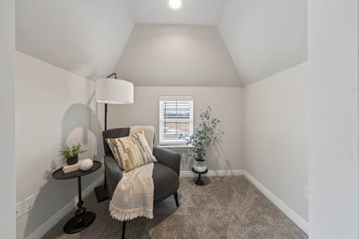 A cozy room with a grey armchair, a small table with a lamp, and a window with a view.