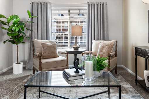 A living room with a glass coffee table and two chairs.