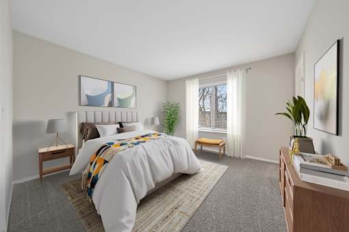 A bedroom with a large bed, a nightstand, a desk, and a window with a view of trees outside.