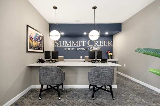 Two grey chairs are placed in front of a desk with a Summit Creek sign on the wall.