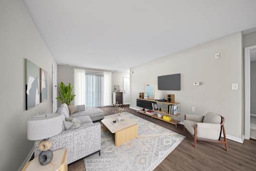 A modern living room with a grey sofa, a wooden coffee table, a white armchair, and a TV on the wall.