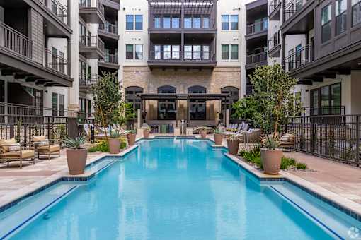 A large swimming pool in the middle of a courtyard surrounded by potted plants and chairs.