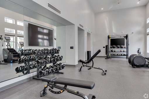 A spacious gym with a variety of equipment including dumbbells, weight plates, and a bench press.