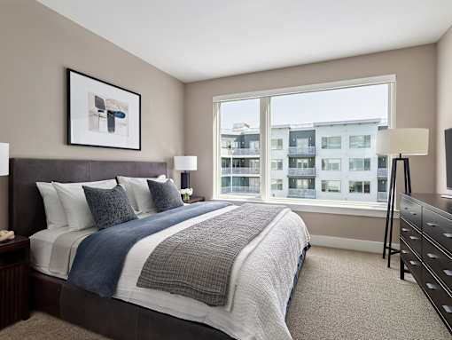 A bedroom with a large bed and a view of a building outside the window.