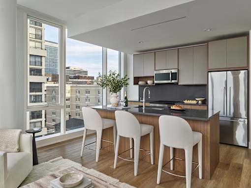 A modern kitchen with white chairs and a view of the city.