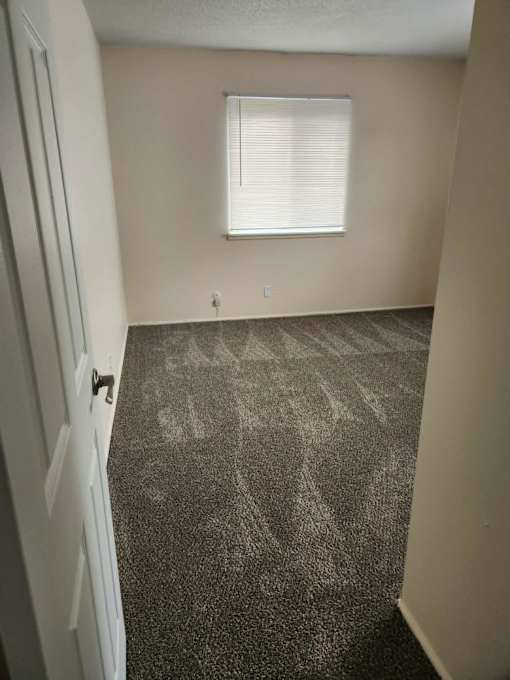 A room with a carpeted floor and a window with blinds.