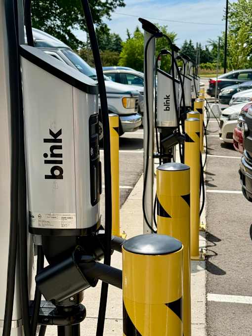 A row of Blink charging stations are lined up in a parking lot.