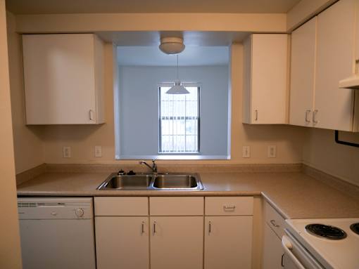A kitchen with a white dishwasher, sink, and stove.