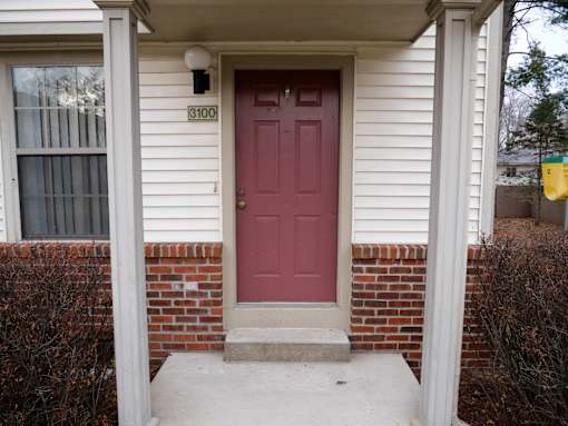A white house with a red door and a mailbox on the wall.