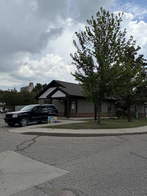 A black car is parked in front of a house with a sign in front of it.