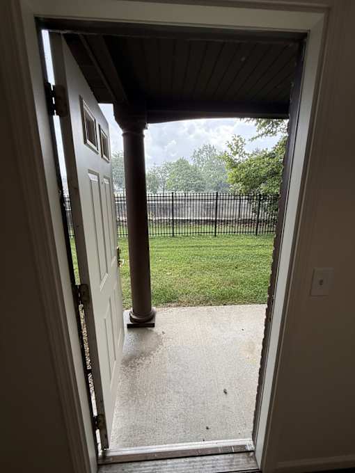 A white door is open to a porch with a black railing.
