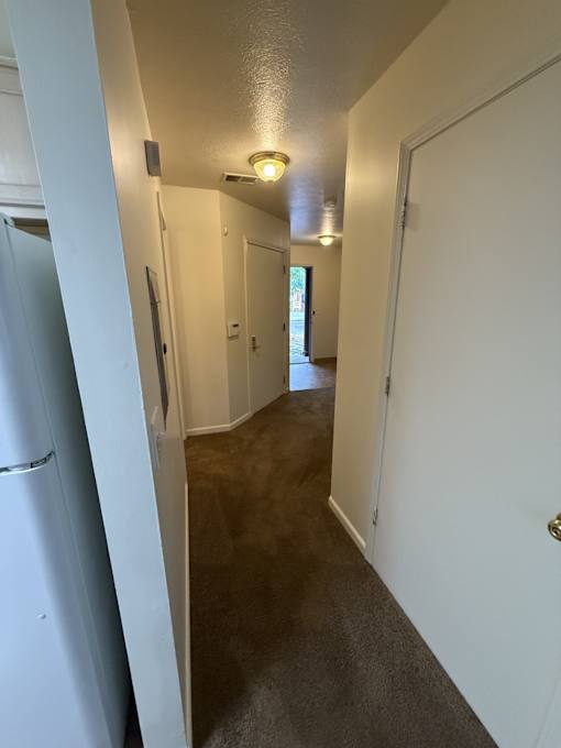 A long hallway with white walls and a refrigerator on the left.