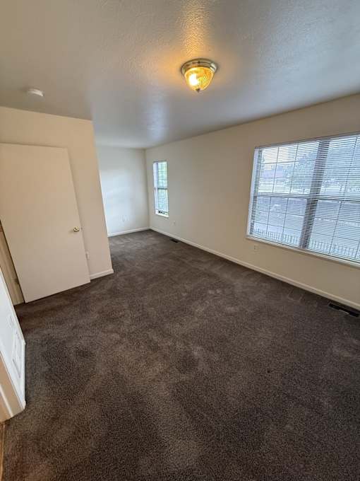 A room with a carpeted floor and a window with blinds.