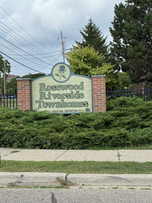A sign for Rosewood Riverside Townhomes is displayed in front of a fence.