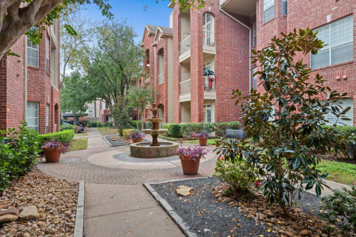 a fountain sits in the middle of a walkway in front of apartment buildings