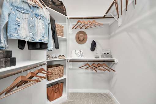 A closet with clothes and a hat hanging on the wall.