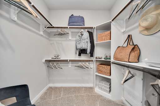 A white closet with clothes and a hat hanging on the wall.