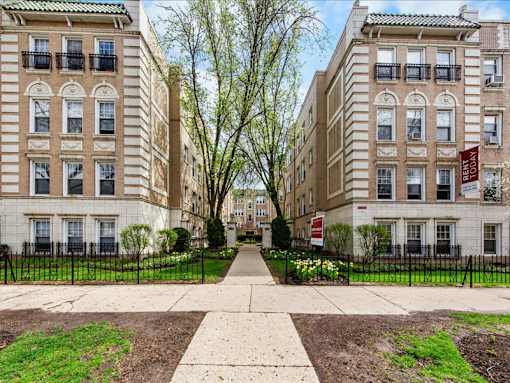 A row of brown and beige apartment buildings with green lawns in front.