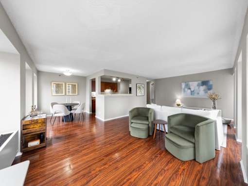 A room with wooden floors and white walls has a dining table and chairs.