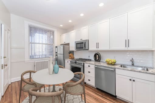 a kitchen with white cabinets and stainless steel appliances and a small table with four chairs