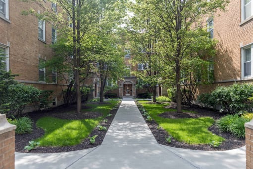 a walkway with trees and grass in front of an apartment building