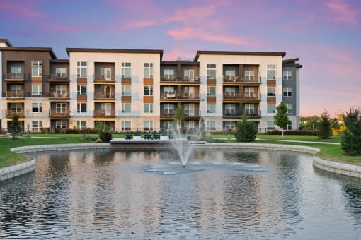 a fountain in a pond with an apartment building in the background