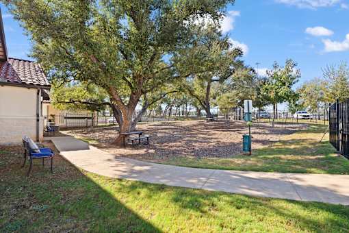 a sidewalk leading to a park with a tree and a bench