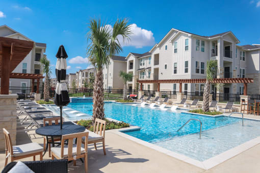 a swimming pool with lounge chairs and umbrellas in front of an apartment building