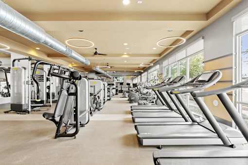a gym with cardio equipment and large windows