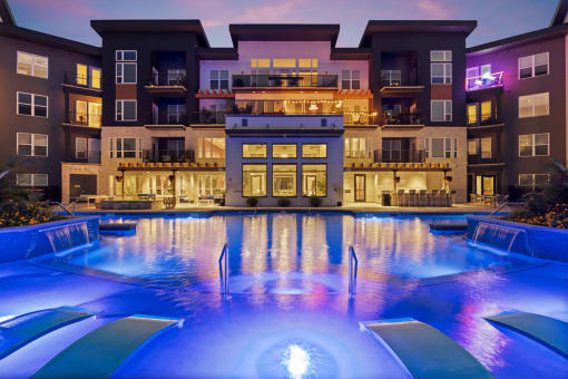 a swimming pool at night in front of an apartment building