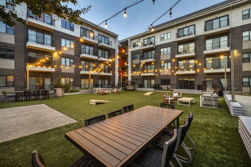 a patio with a wooden table and chairs on a lawn in front of an apartment building