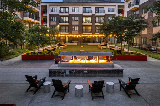 an outdoor patio with chairs and a fire pit in front of an apartment building