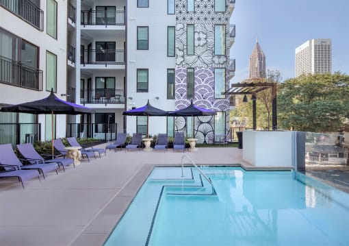 a swimming pool with chairs and umbrellas in front of an apartment building