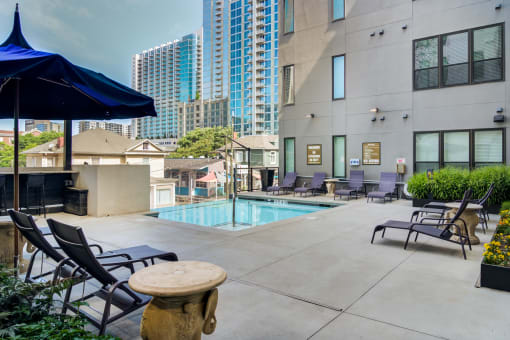 a swimming pool with lounge chairs and umbrellas at a building with tall buildings
