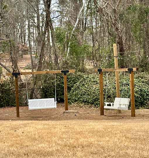 Two wooden swing sets in a field with trees in the background.