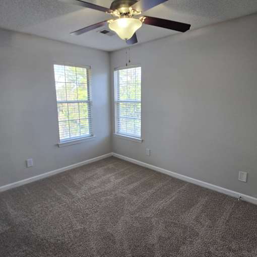 A room with a ceiling fan and two windows.