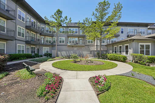 A courtyard with a circular walkway and a small garden in the middle of apartment buildings. at Highline Urban Lofts Apartments, Cypress, TX, 77429
