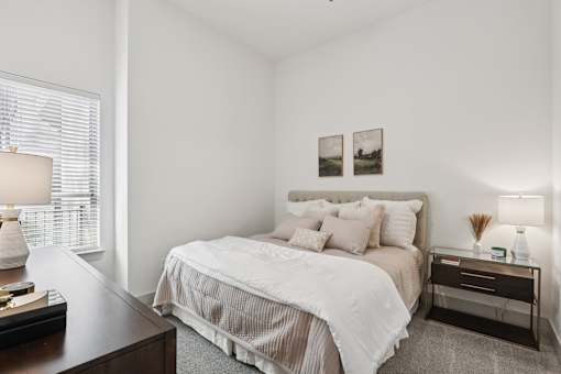 A bedroom with a large bed and a nightstand with a lamp at Everra Midtown Park Apartments, Dallas