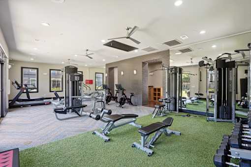 A well-equipped gym with a variety of exercise machines and a green artificial turf area at Highline Urban Lofts Apartments, Cypress, Texas