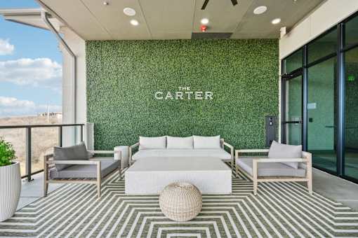 A white sofa and two chairs are arranged on a striped rug in front of a green wall with the word "CARTER" on it.