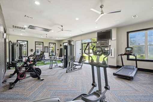 A spacious gym with a variety of equipment including treadmills, elliptical machines, and a television at Highline Urban Lofts Apartments, Cypress