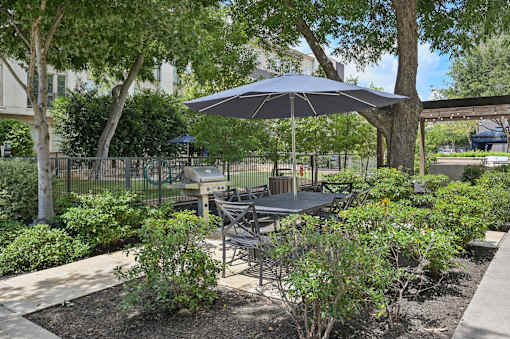A patio with a table and chairs under an umbrella at Everra Midtown Park Apartments, Dallas, TX, 75231