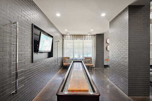 A long hallway with a shiny wooden table in the middle and a television on the wall at Highline Urban Lofts Apartments, Texas, 77429