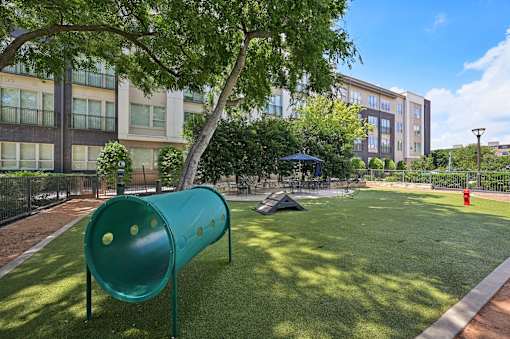 A playground with a green slide and a tent in the background at Everra Midtown Park Apartments, Dallas, TX, 75231